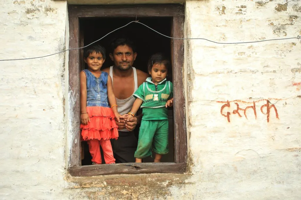 The image shows a father posing with his two young children as they stand in a window frame of their home.