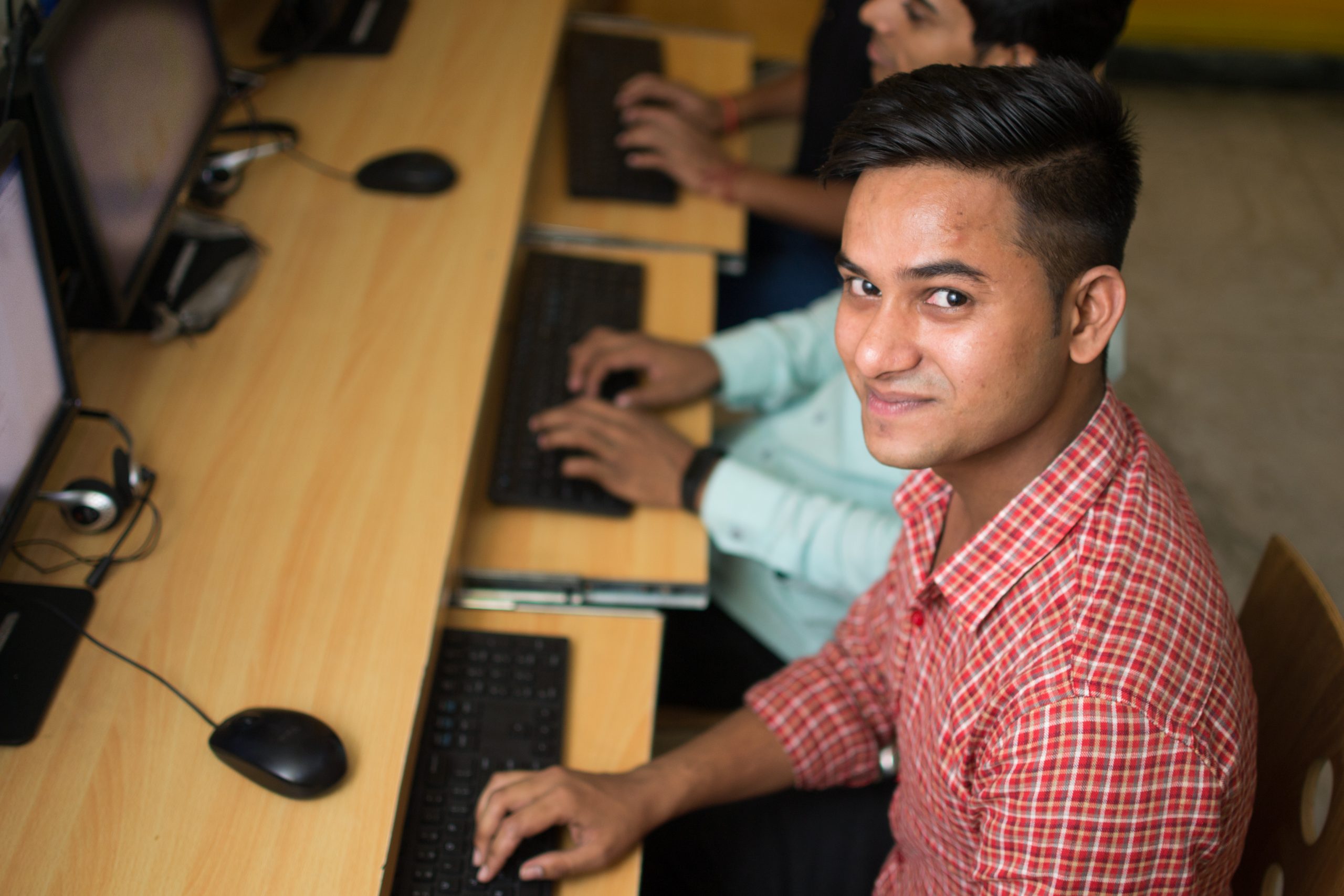 Young boy in checked shirt, sitting at computer, looks up into the camera