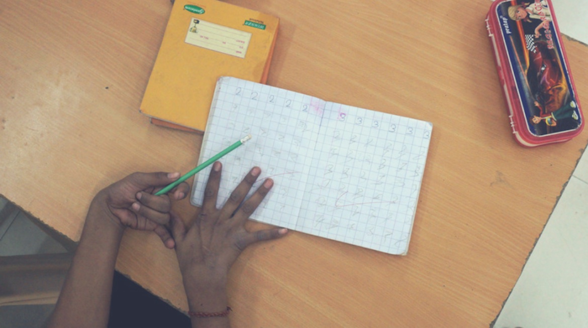 A child with disability holding a pencil over an open notebook in what looks like a school setting