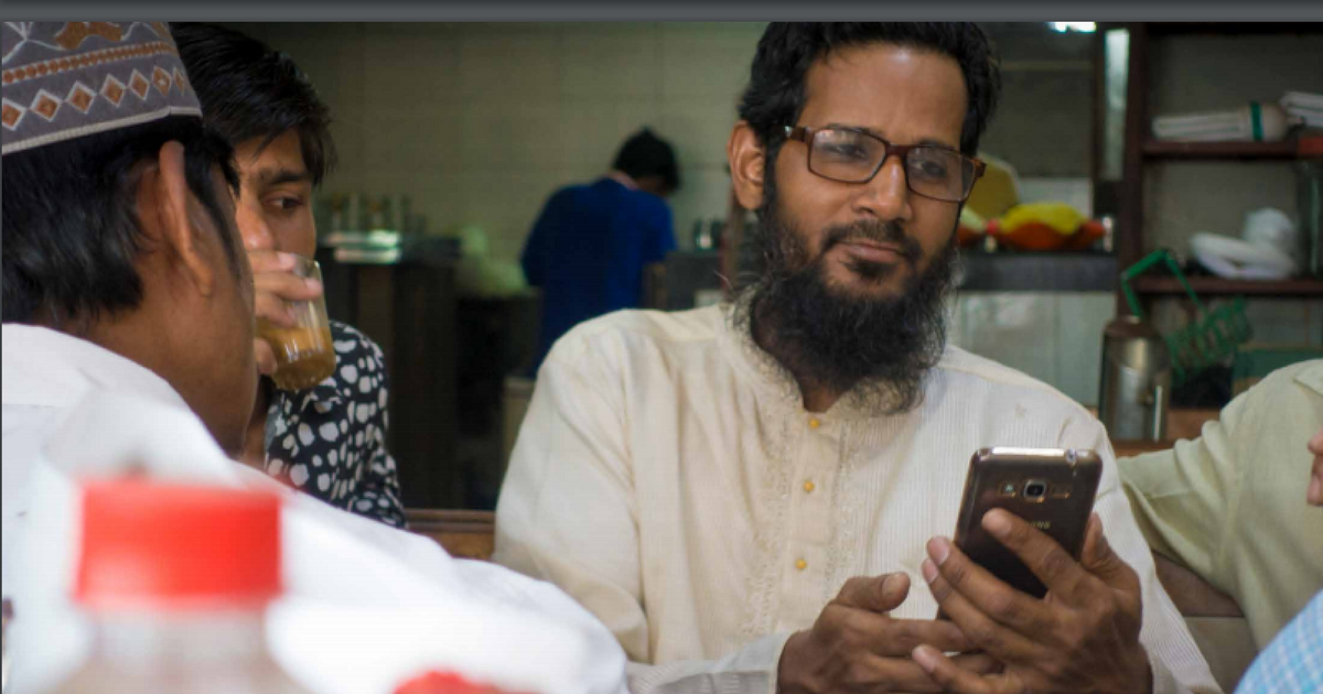 one man looking at his smartphone, another one drinking tea