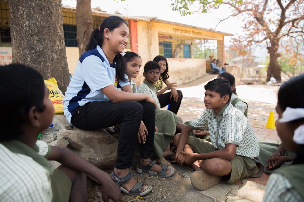 Magic bus teacher sitting with students near a tree - corporates