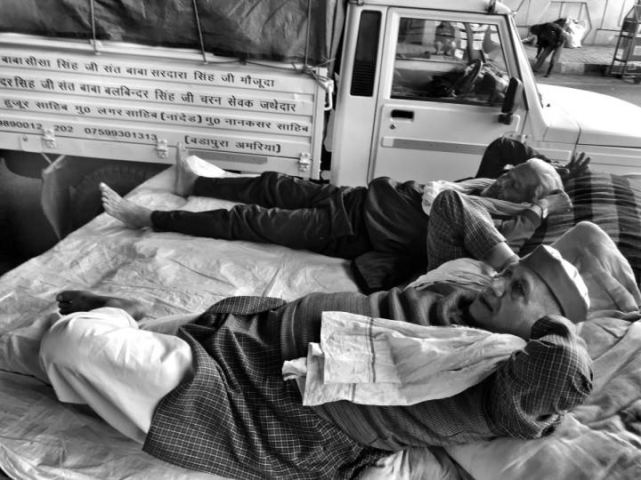 Two older men lying on the back of a truck next to each other-farmers protest