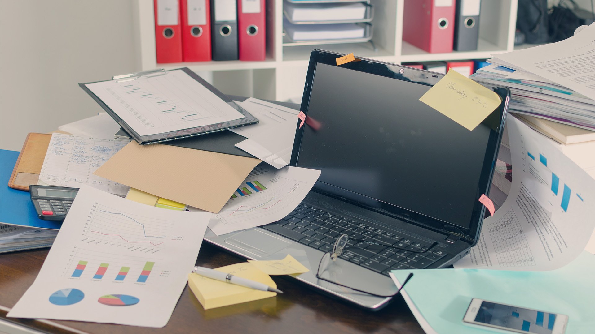 A cluttered desk with a laptop and data sheets