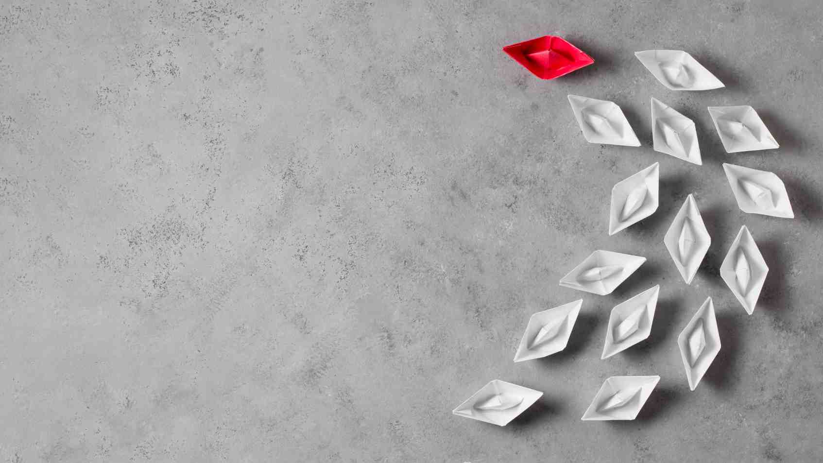 White paper boats following a red paper boat