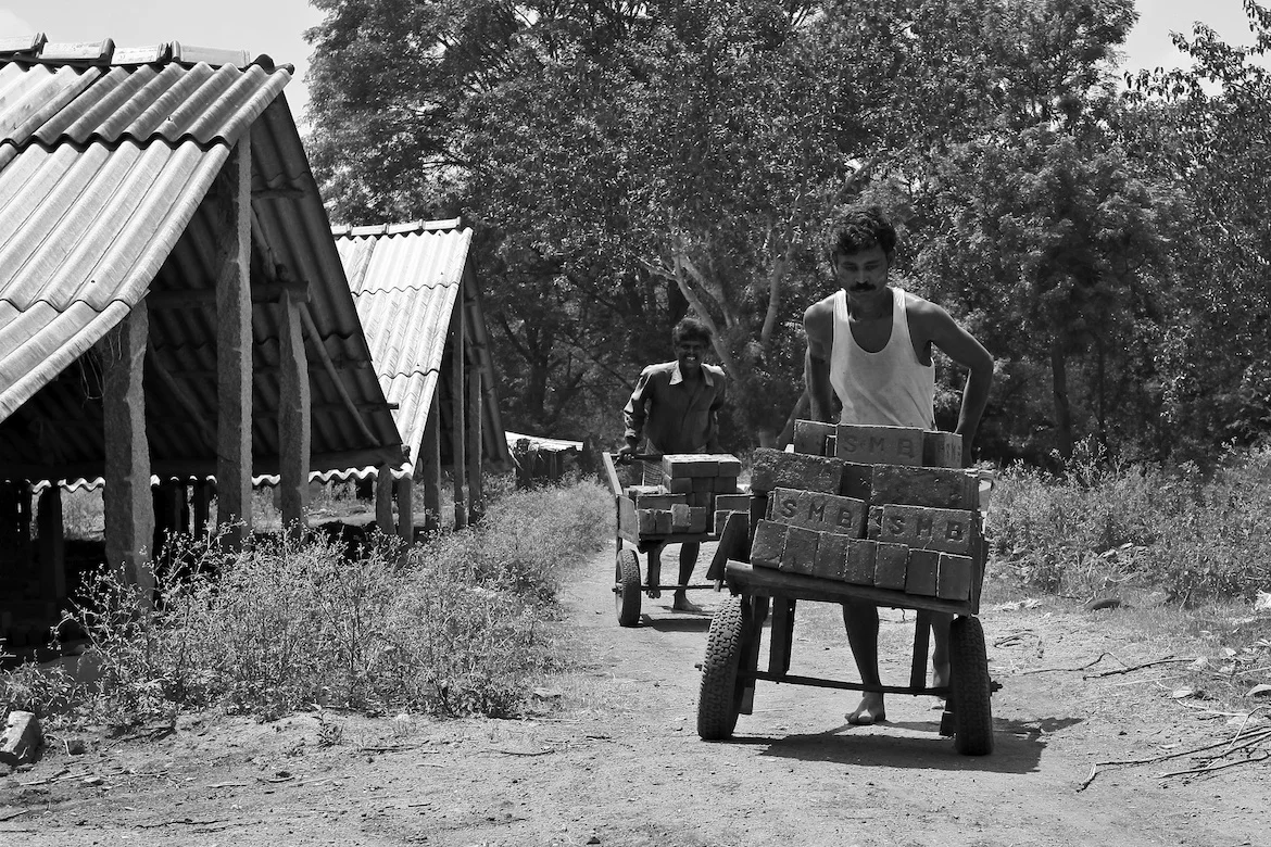 two men carrying bricks on a cart