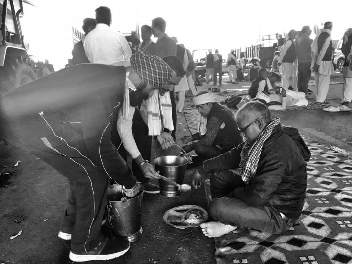 People seated in a row on the ground being served food by people-farmers protest