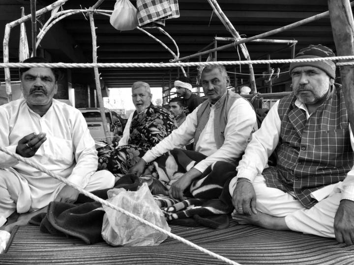 People sitting on the road behind a rope barricade looking into the camera-farmers protest