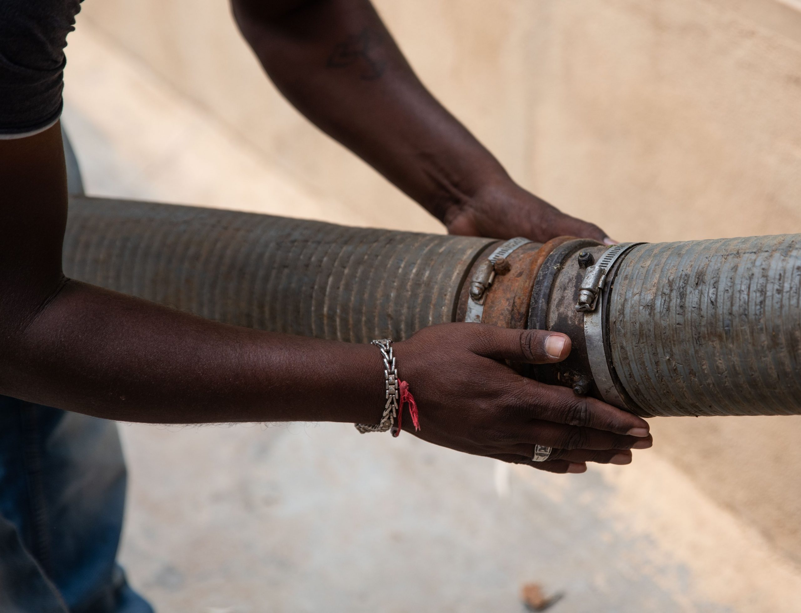 Men holding sewage pipe with bare hands_sanitation workers_epw