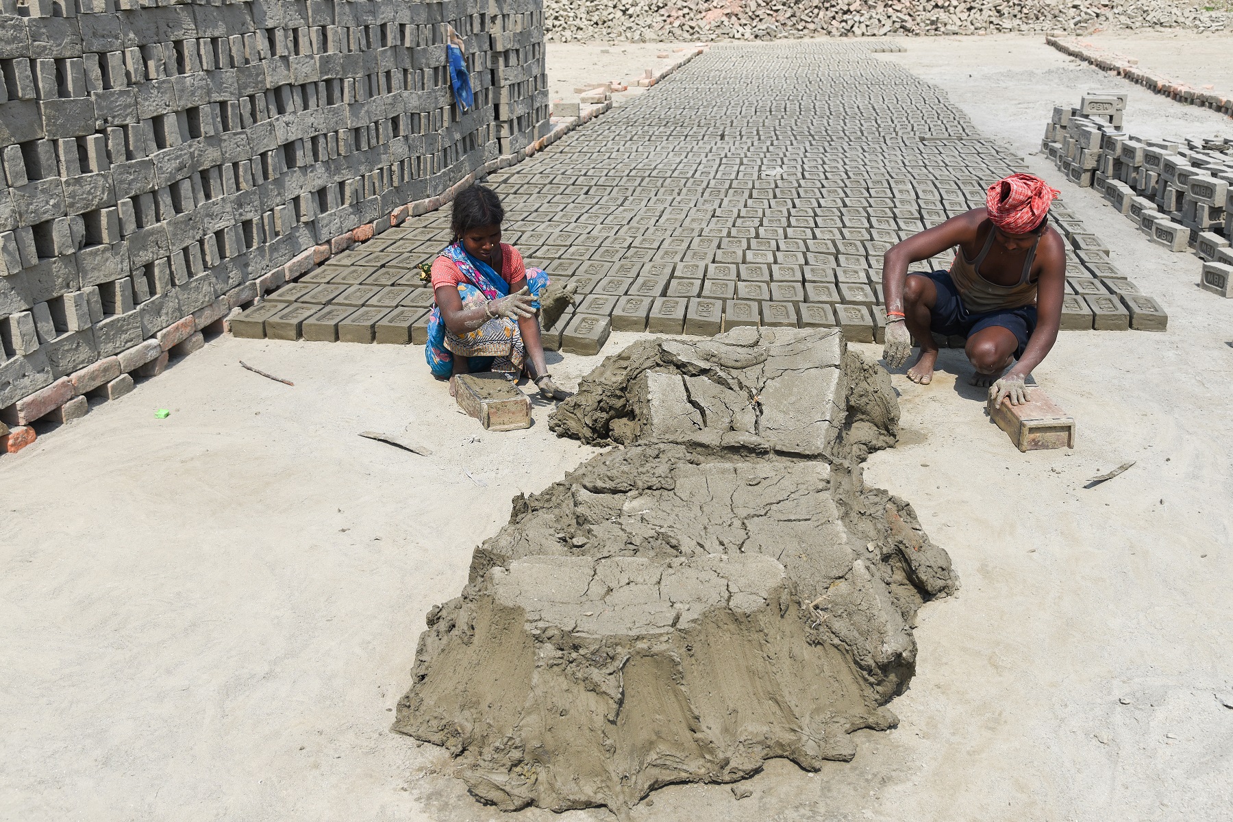 A young Indian girl and man making bricks out of clay at a brick kiln