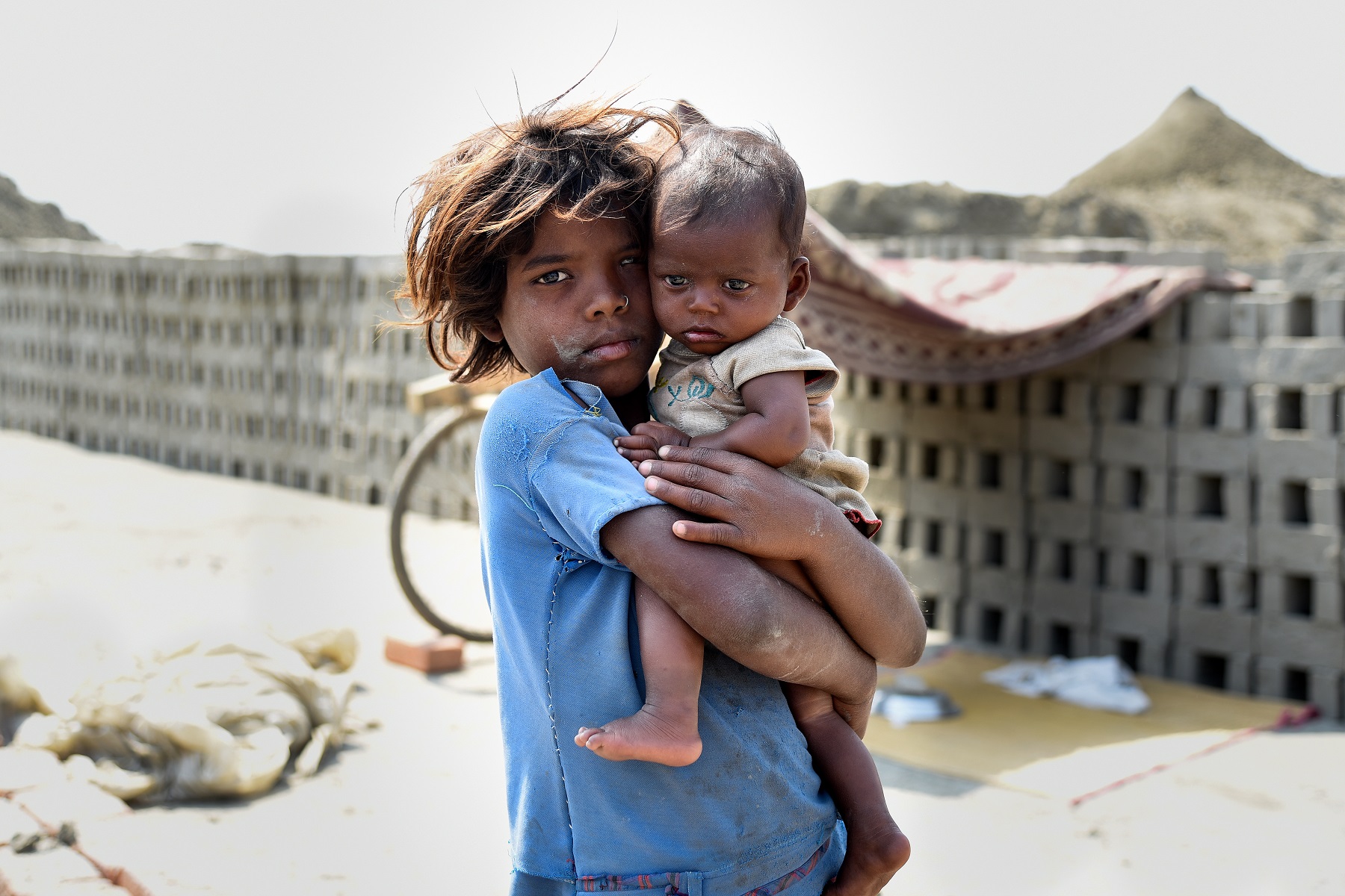 A young Indian girl with her baby sibling in her arms at a brick kiln