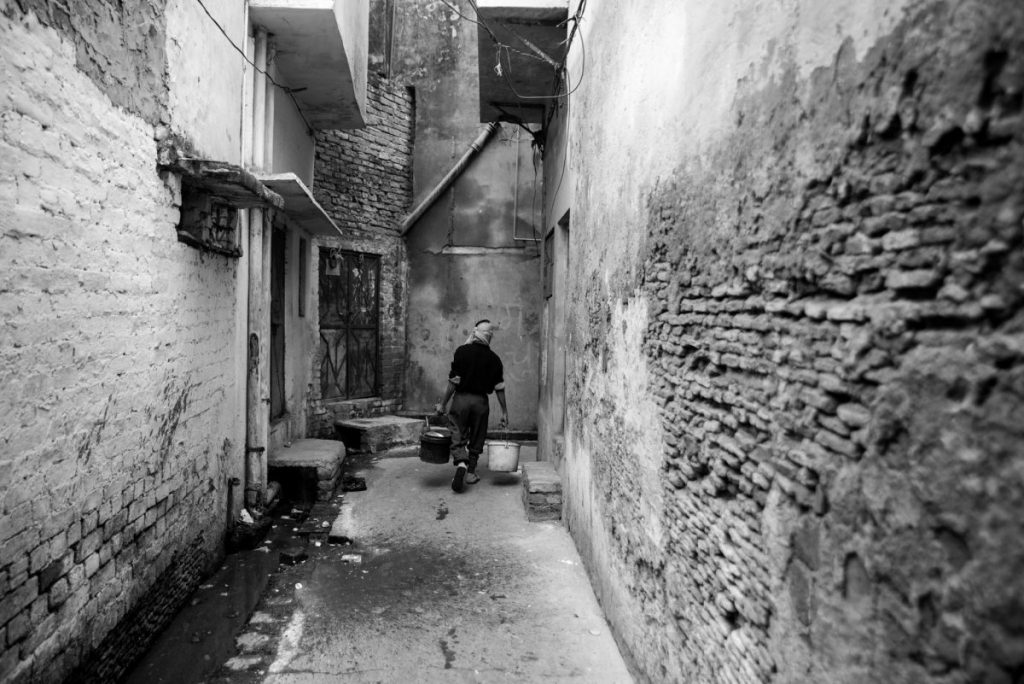 man carrying buckets of waste in an alley