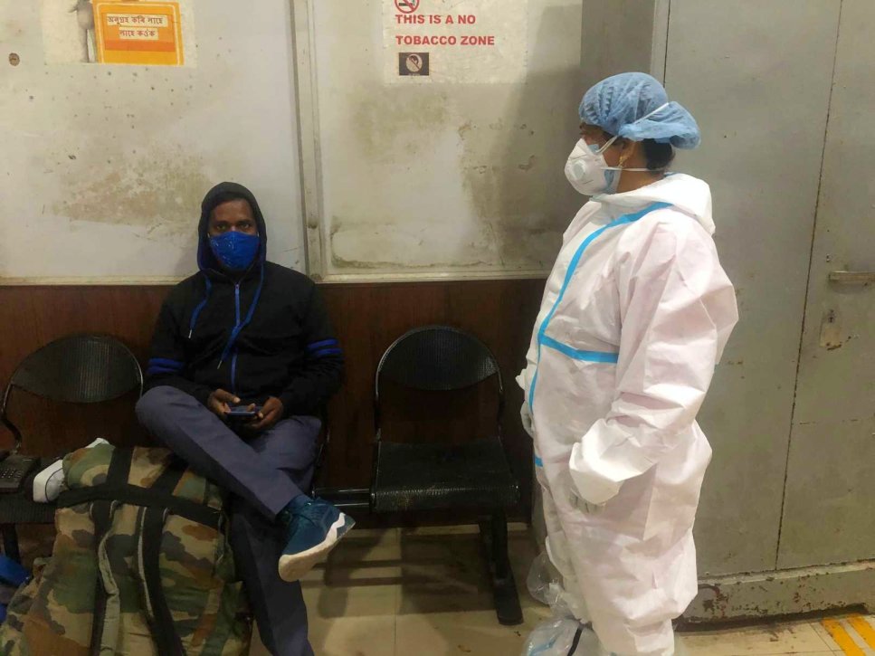 Manika Mandal wearing a PPE standing next to a seated masked man-ward worker