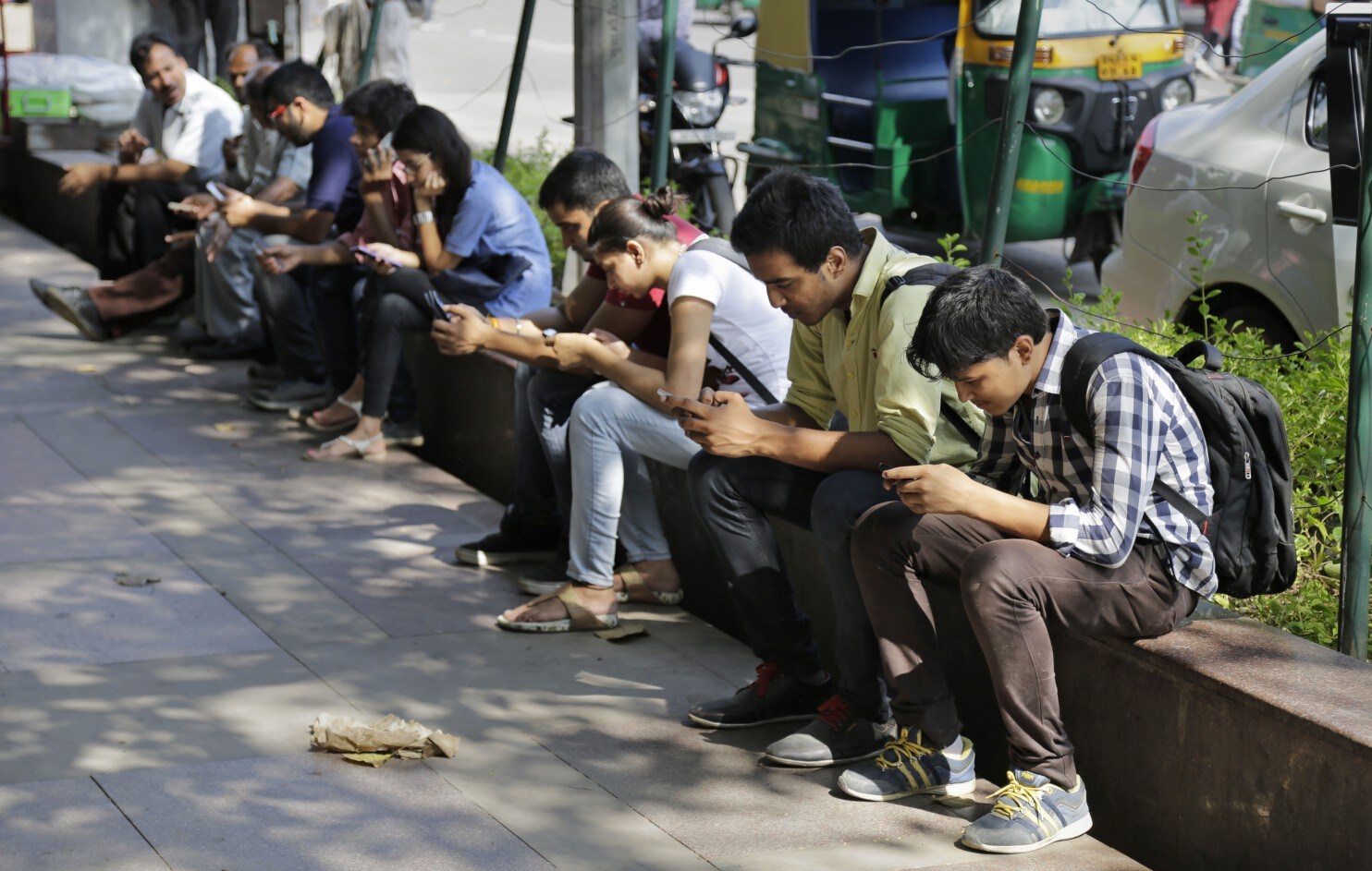 Young adults sitting on a bench looking down at their smartphones _ India