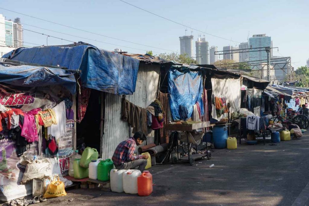 Image 3_ Person sitting on top of water containers at the entrance of a slum-water for all-picture courtesy- Suraj Katra