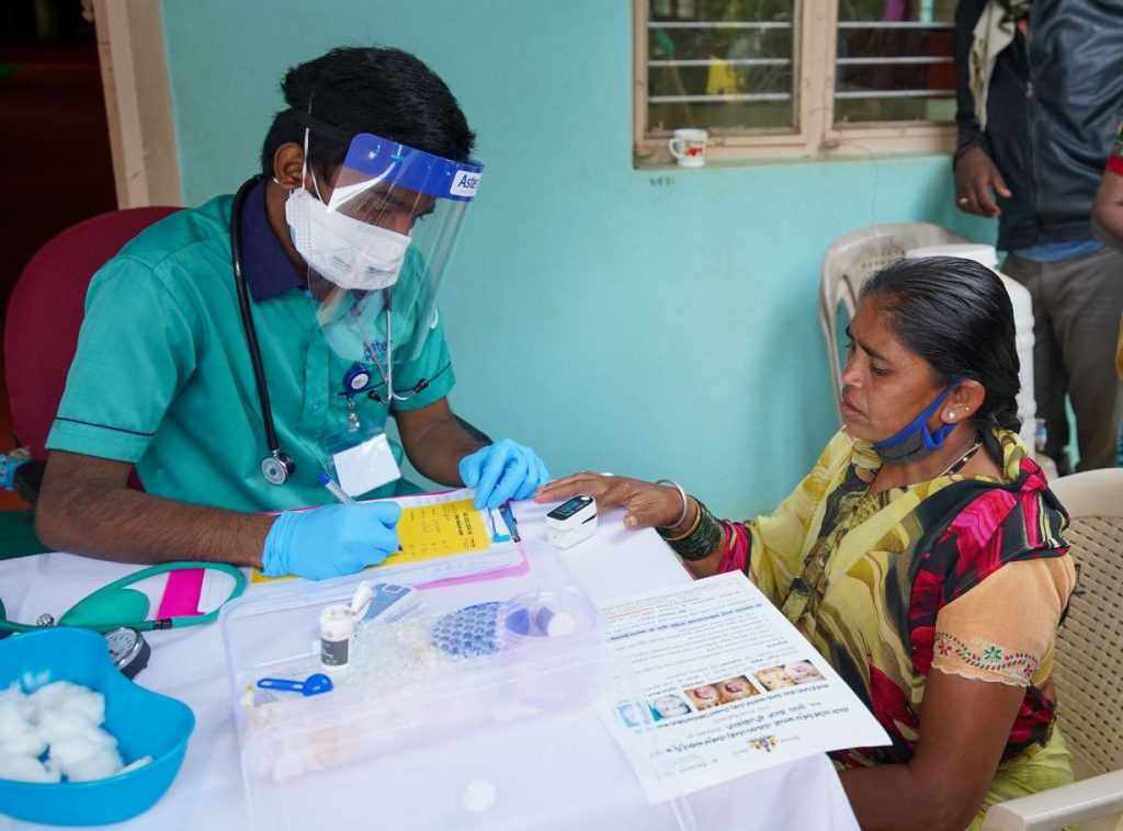 A woman getting her oxygen levels checked by a person wearing a mask and face shield_COVID-19_second wave_vaccine hesitancy_picture courtesy: Trinity Care Foundation/Flickr