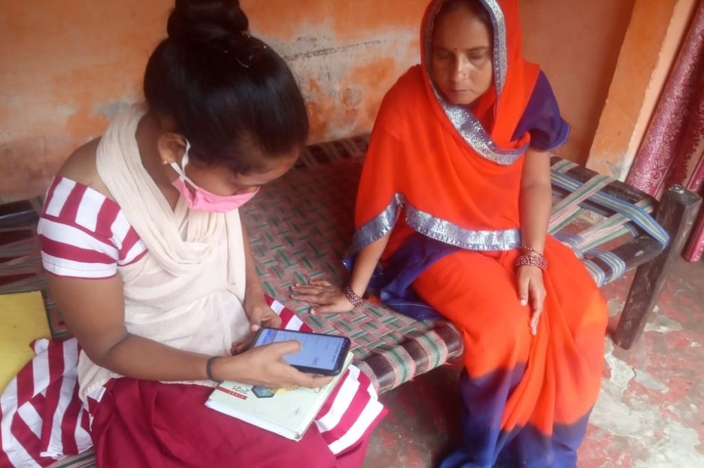 A woman wearing an orange saree watching a girl wearing a mask operate a mobile phone. The article that funders in the social sector have an incredible opportunity and obligation to change our one-way relationship with data.