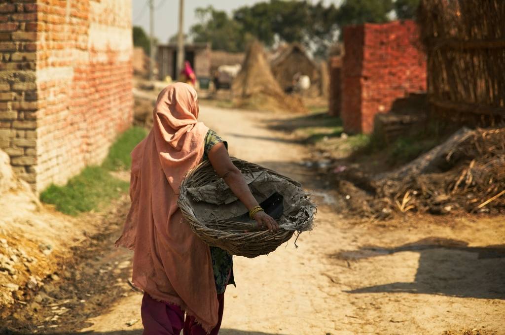 the back of a women holding an empty waste basket against the backdrop of an empty street lined with brick buildings-manual scavengers