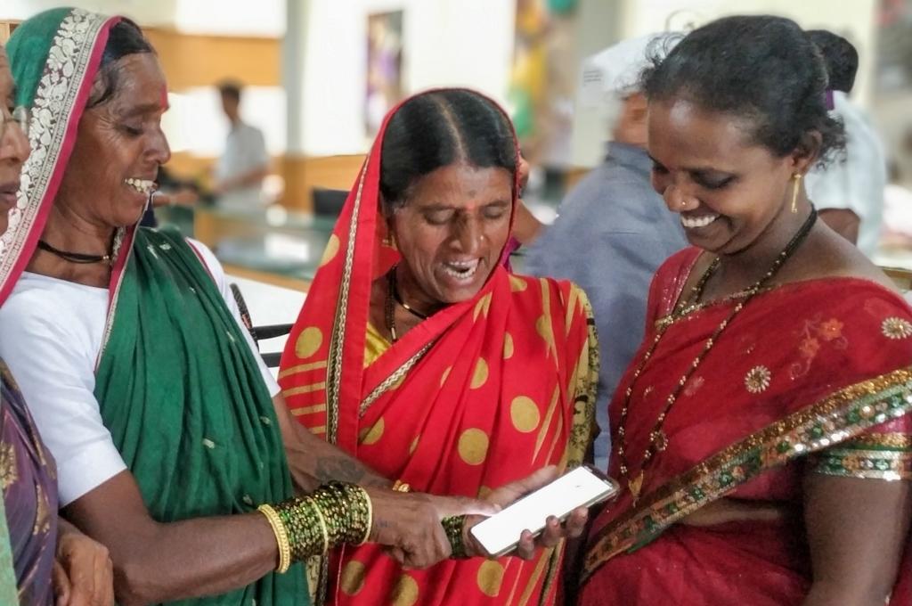 three women looking at a smartphone and smiling-women entrepreneurs micro enterprises