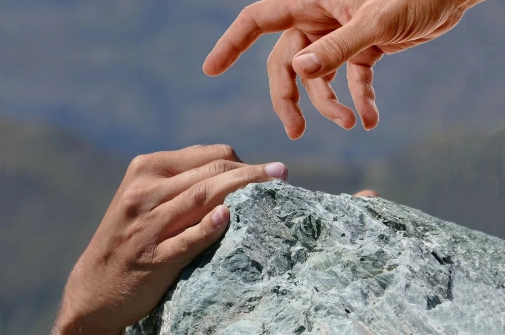 A hand reaching out to hold another on a rock. Budget 2022 can encourage citizens to donate to nonprofits