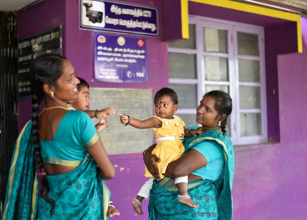 Two women heathworkers standing and talking to each other while also holding kids on their lap