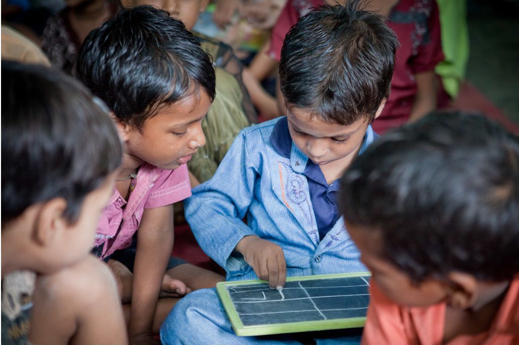 Children huddled over a small blackboard as one of them draws on it with a chalk-education