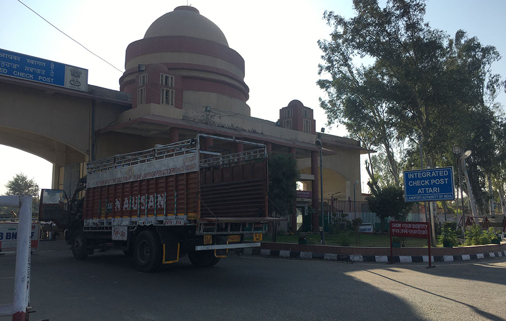 An empty truck stopped at check post that is attached to a building. A sign reads, "Integrated Check Post Attari"._Attari-wagah border