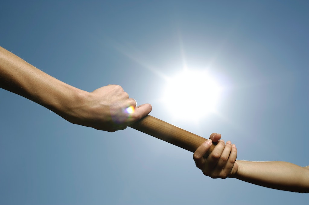 One hand passing a baton to another_leadership transition