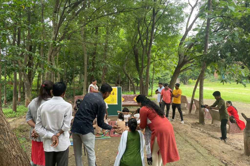 A group of people shooting a teacher teaching students in a open field_Adivasi communities