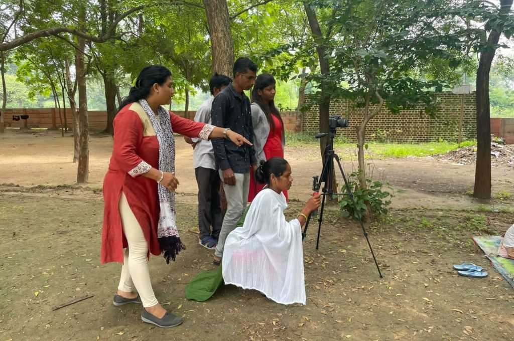 A woman shooting on a camera with people standing around her_Adivasi communities