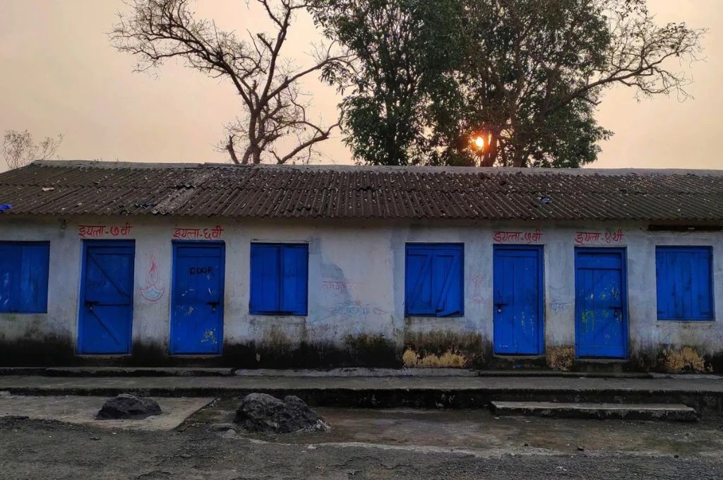 The image features an anganwadi centre. It is a small, single-storey structure with four doors. Two of the doors are labelled class 6th and 7th respectively._nutrition