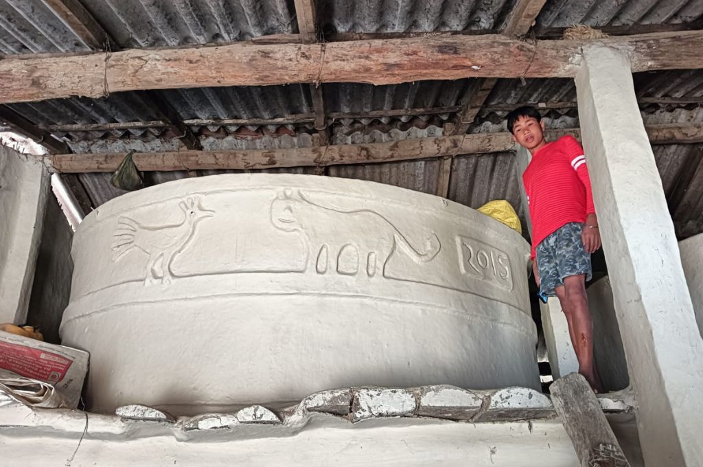 a boy stands next to a granary with animals engaved on its walls--tharu tribe