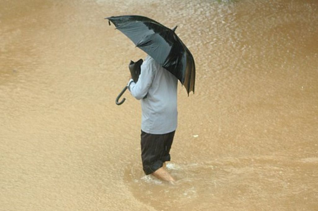 a man with an umbrella standing in a flooded area--climate change adaptation