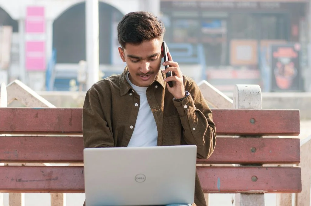 a young indian man working on his laptop while taking a phone call--tech tools