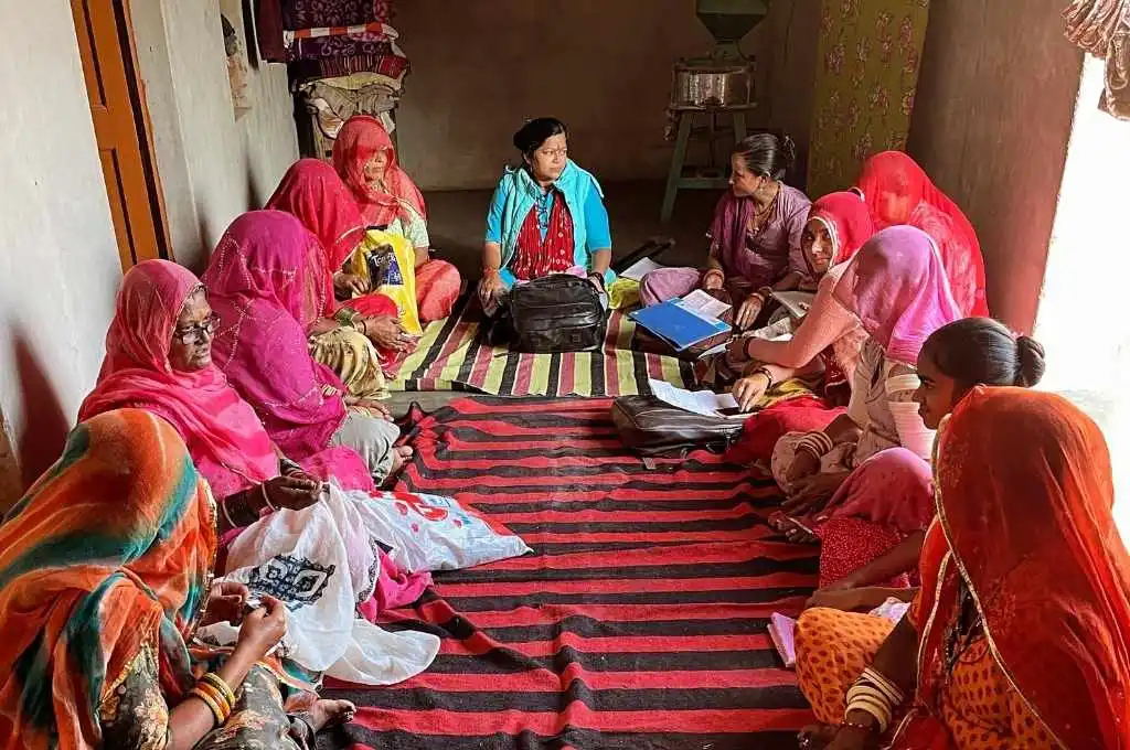 a group of women sitting on the ground being surveyed-enumerator