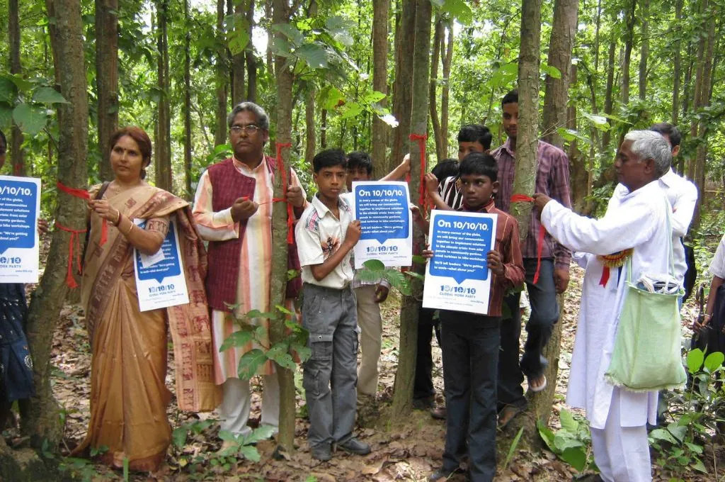 A group of people stand in a forest holding signs. - Forest Rights Act