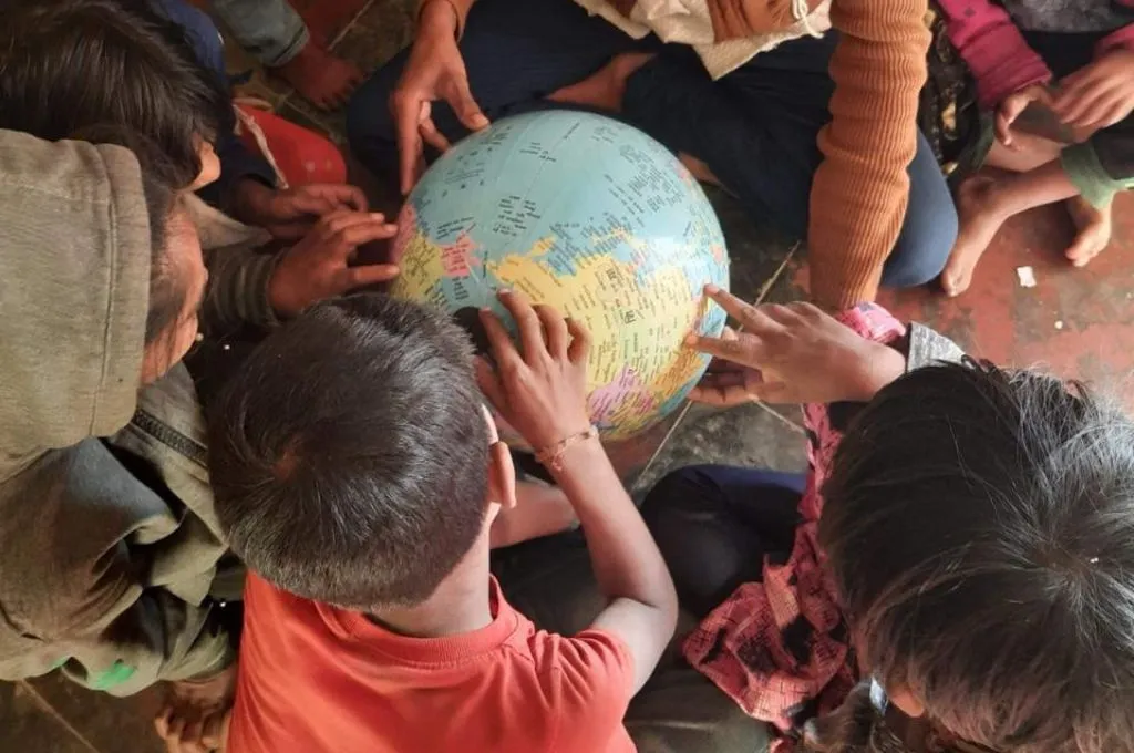 The image features a group of children sitting in a circle. There is a model of a globe in the middle and the children are pointing at different locations._Rights-based development