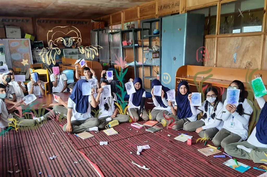 Students seated in circle proudly display their colourful artwork_community engagement