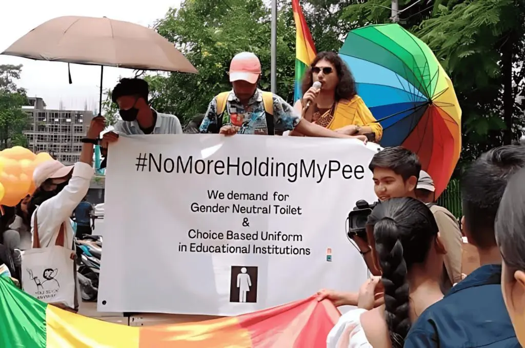 The image features an event from Akam Foundation's No More Holding My Pee campaign. The author, Rituparna, is joined by 2 other people and they are holding a sign with the text, 'No More Holding My Pee. We demand for gender neutral toilet and choice-based uniform in educational institutions'._Queer inclusion