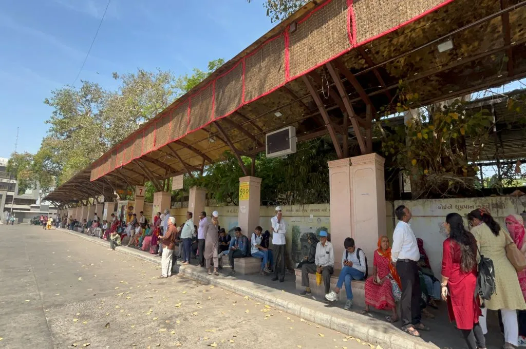 Many people standing in the shade under a bus stop-heat communication