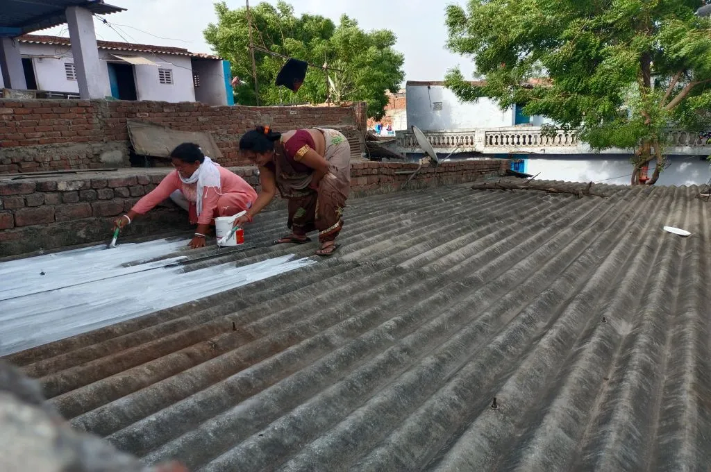 Two women painting a roof with solar-reflective white paint-heat communication