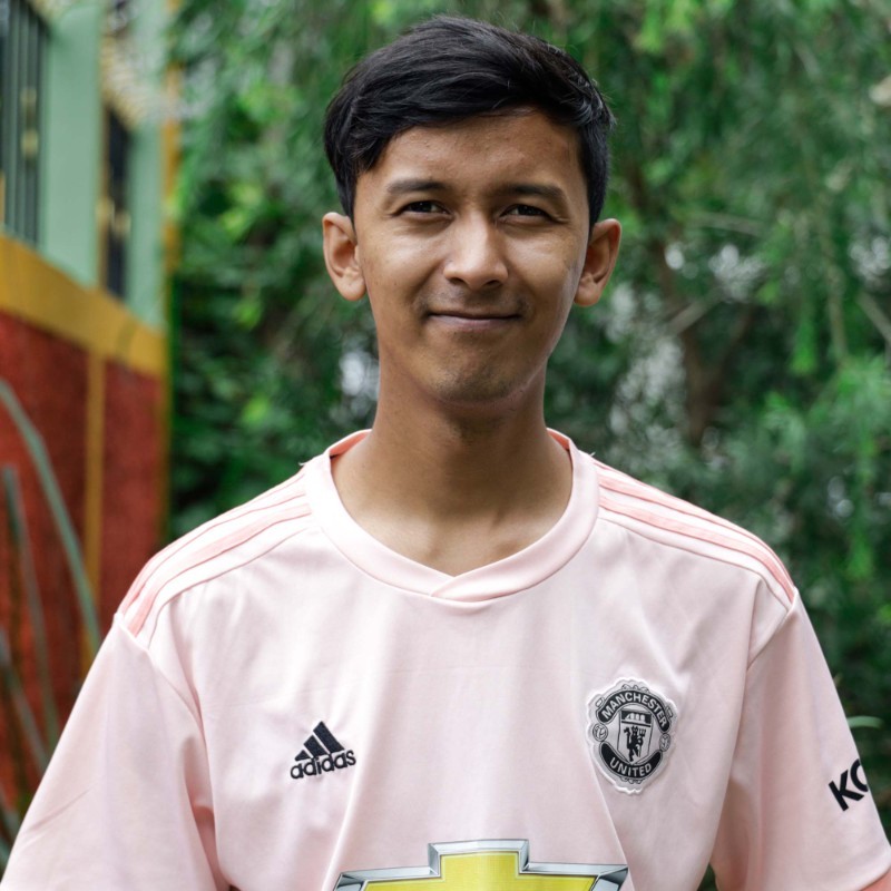 A boy wearing a pink Manchester United jersey against the backdrop of greenery