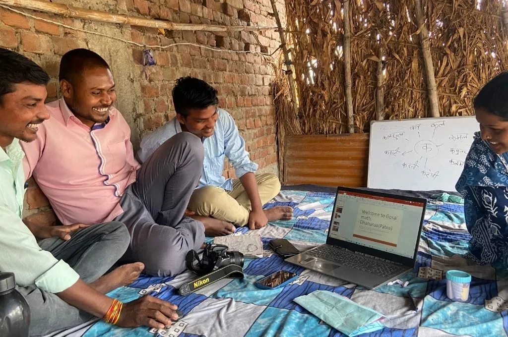 three men and a woman look at a presentation on a laptop, smiling--musahar education