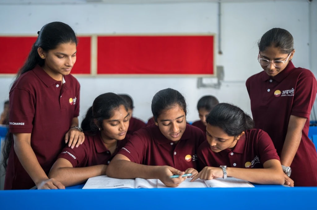 five girls in a classroom wearing a uniform of red polo t-shirts going over a textbook together--girls in STEM