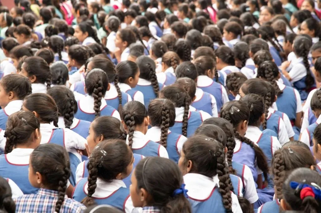 A large group of schoolgirls sitting outdoors in rows, all wearing blue and white uniforms with braided hair--scholarships