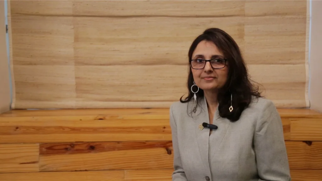 An image of Jaya Dhindaw. She is seated on a wooden bench in front of a beige window shade._Urban planning