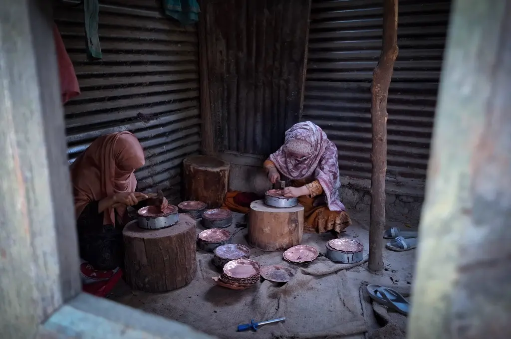 two female coppersmiths wearing headscarves in a workshop in kashmir--coppersmiths