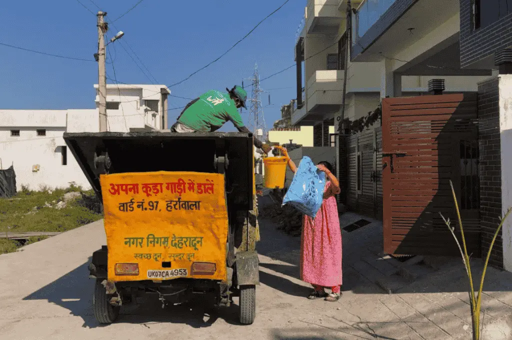 a woman handing over waste to a waste collector wearing a green uniform and standing in a truck in dehradun, uttarakhand--waste management
