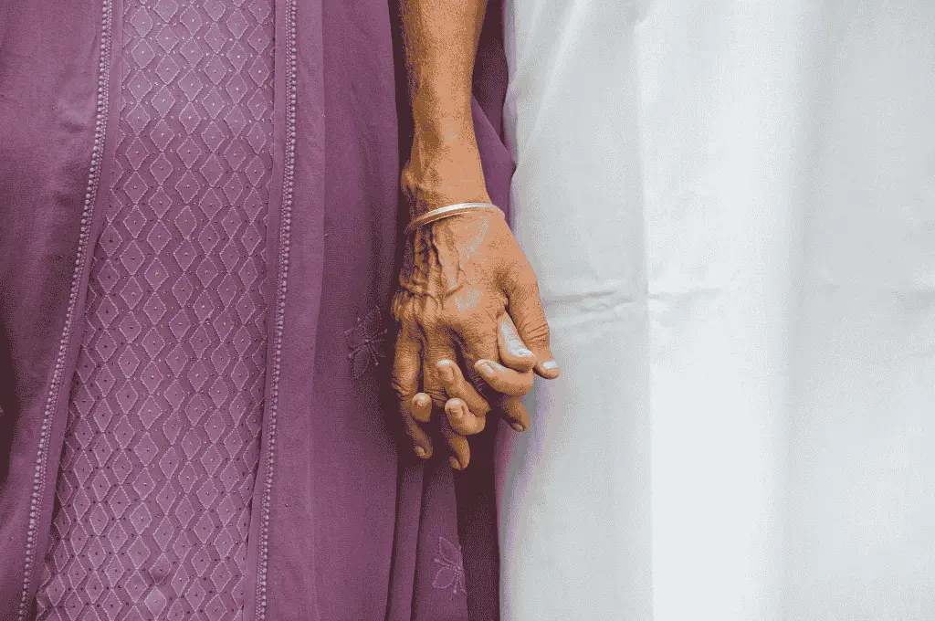 close up of two hands held together, one wearing a bracelet, with one hand in a purple garment and the other in white--intergenerational trauma