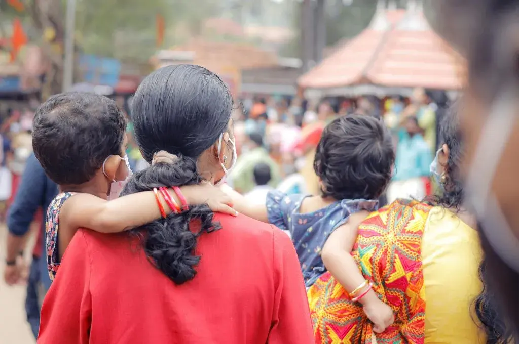 a woman in a red blouse with her back to the camera carrying a child--maternal well-being