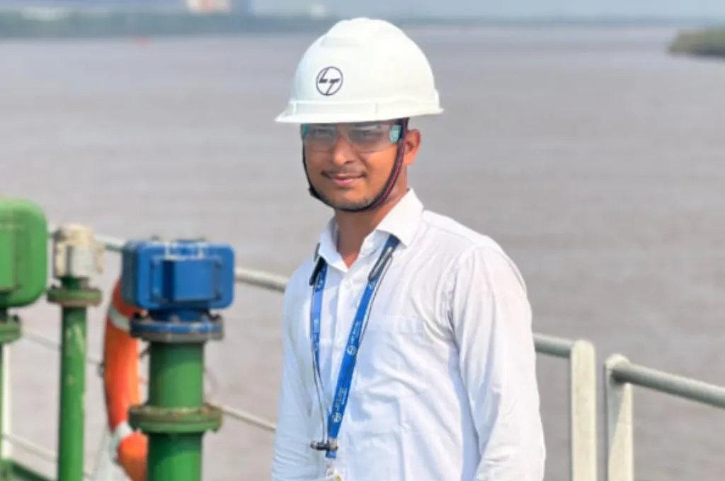 A civil engineer wearing a white helmet, a white shirt, and a lanyard around his neck, with a water reservoir in the background--economic inclusion